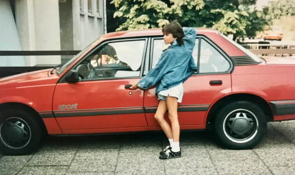 Ein Porträt einer Frau mit dunklen Haaren, die freundlich in die Kamera lächelt. Sie trägt eine Brille mit dunklem Gestell, eine feine Goldkette und ein dunkelblaues Oberteil.